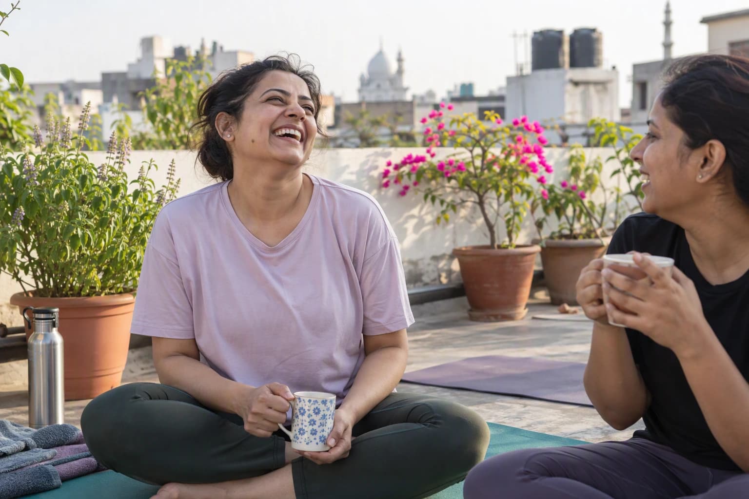 A woman laughs on a rooftop yoga mat with a friend after a morning session