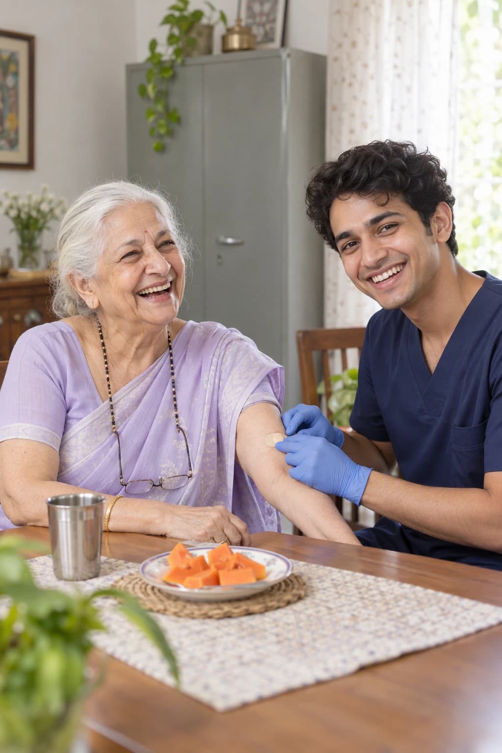 A white-haired woman in her early sixties laughing at her dining table with a young male technician pressing a small plaster to her inner elbow
